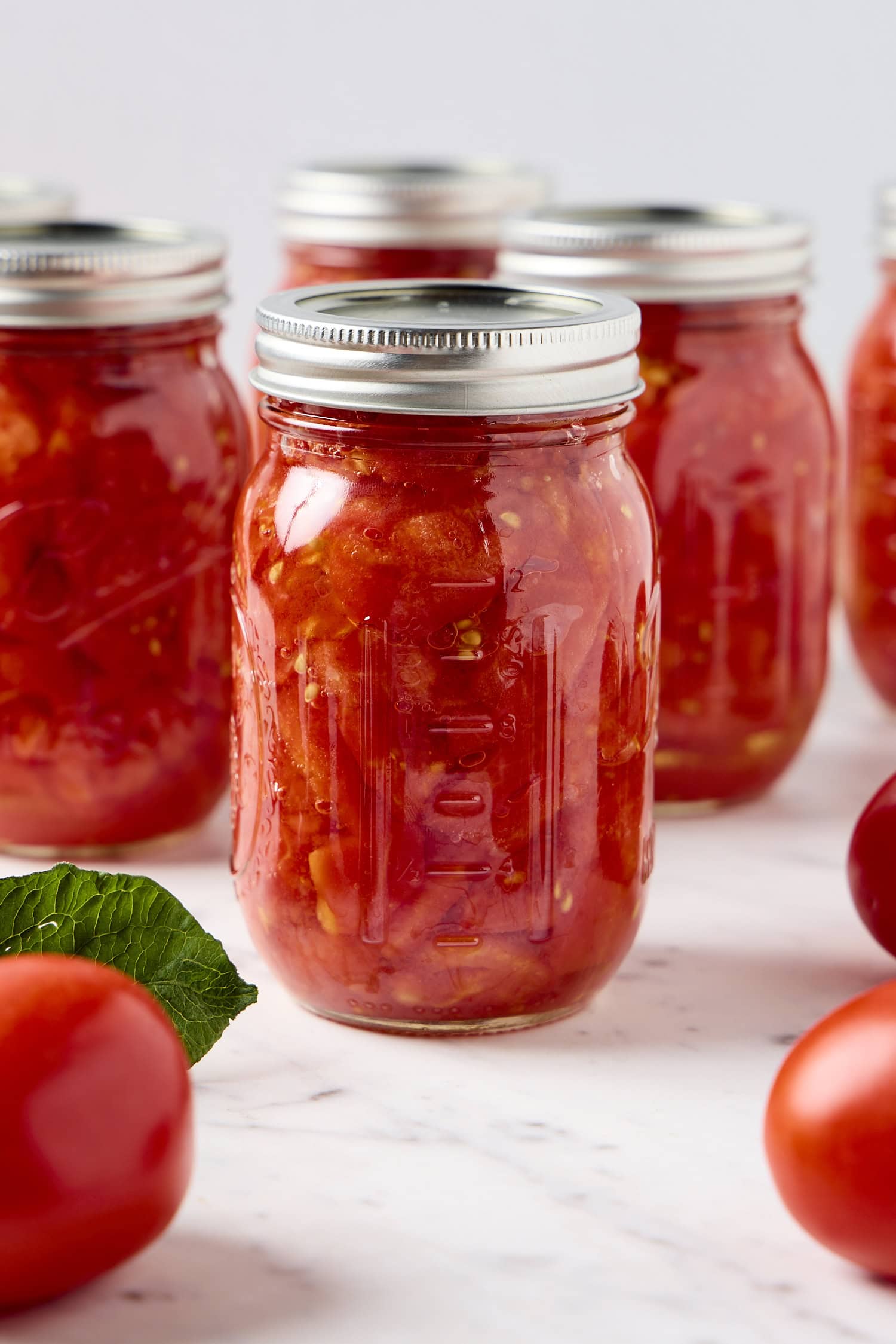 Tomatoes sit next to a glass jar of preserved tomatoes.