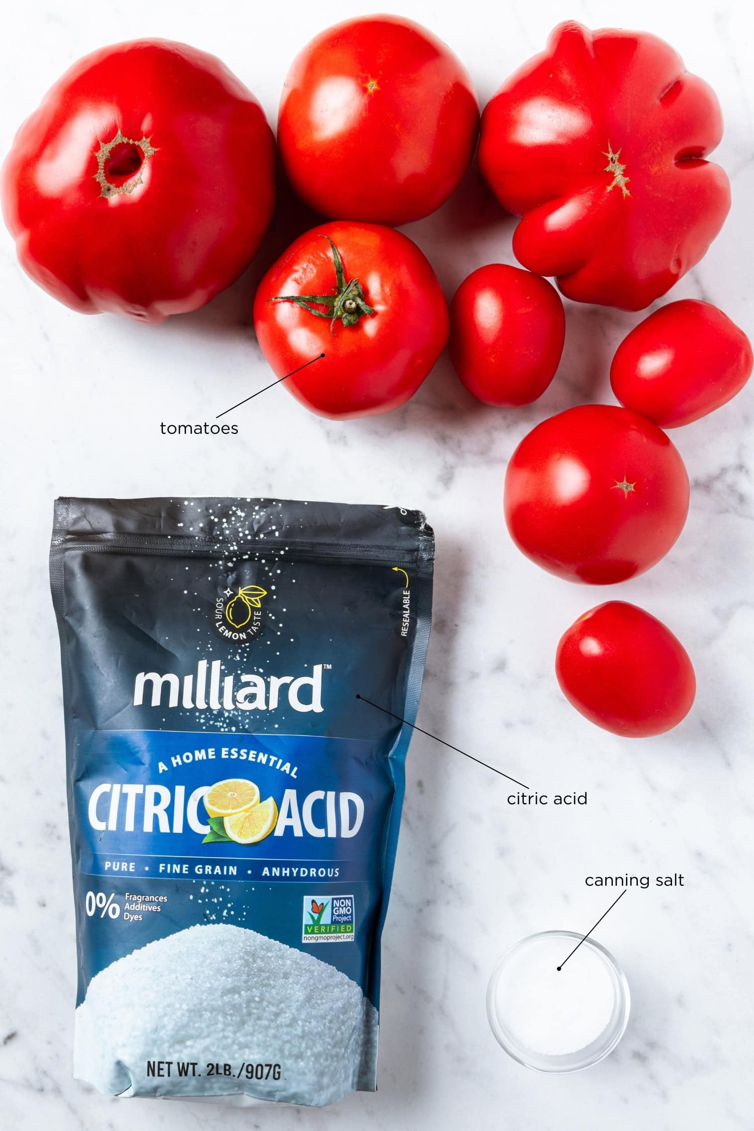 Ingredients to can tomatoes sit on a marble surface. Includes tomatoes, canning salt, and citric acid.