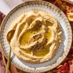 A plate with butternut squash hummus topped with a drizzle of olive oil surrounded by chips.