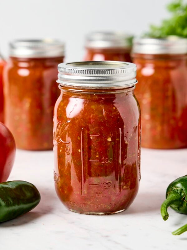 Glass canning jar filled with canned homemade salsa with more jars behind.