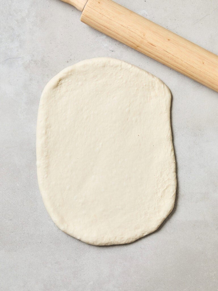 Bread dough being rolled out on a counter.