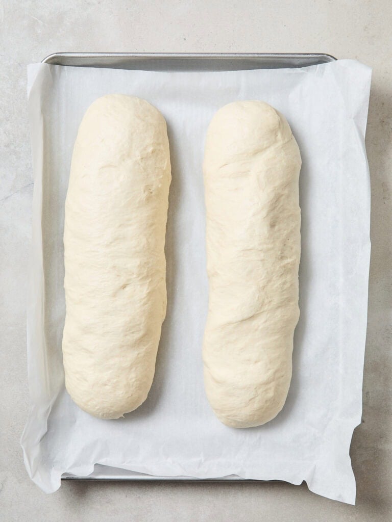 Two loaves of French bread on a baking sheet prior to baking.