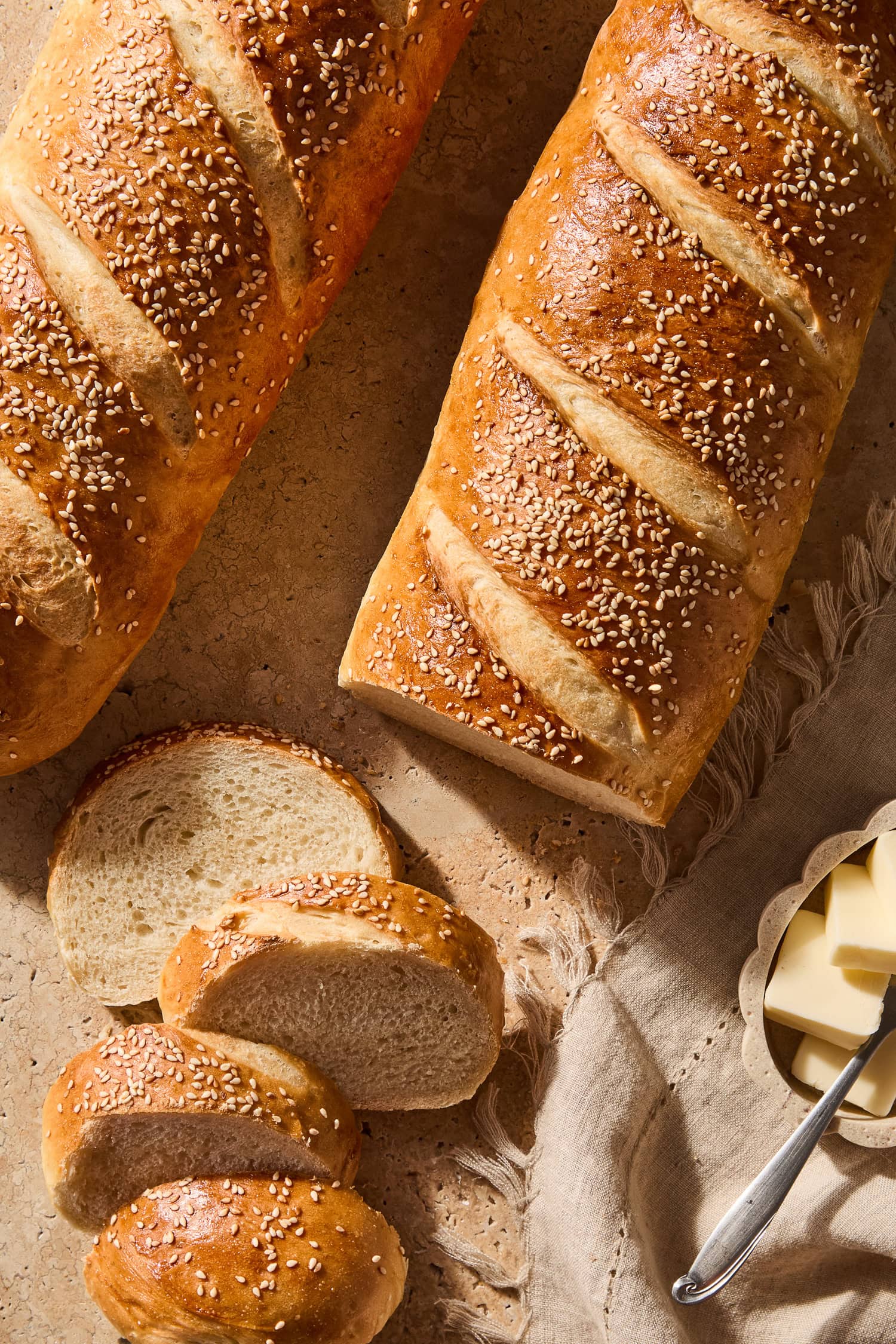 Loaves of French bread being sliced on a countertop next to butter.