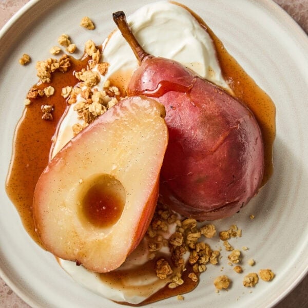 Poached pears sit on top of a bed of Greek yogurt garnished with syrup and granola.