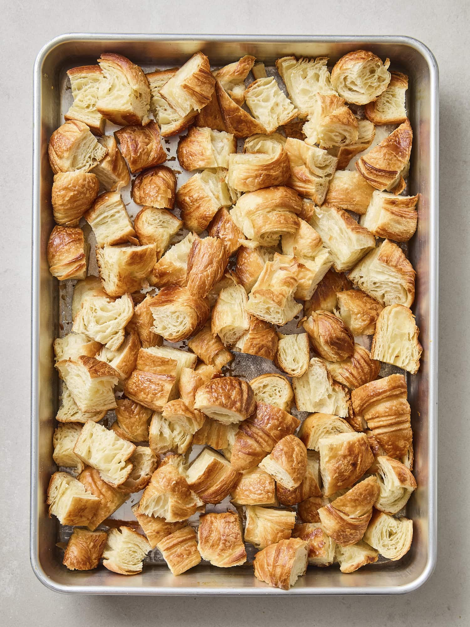 Toasted croissant torn into pieces on a baking pan.