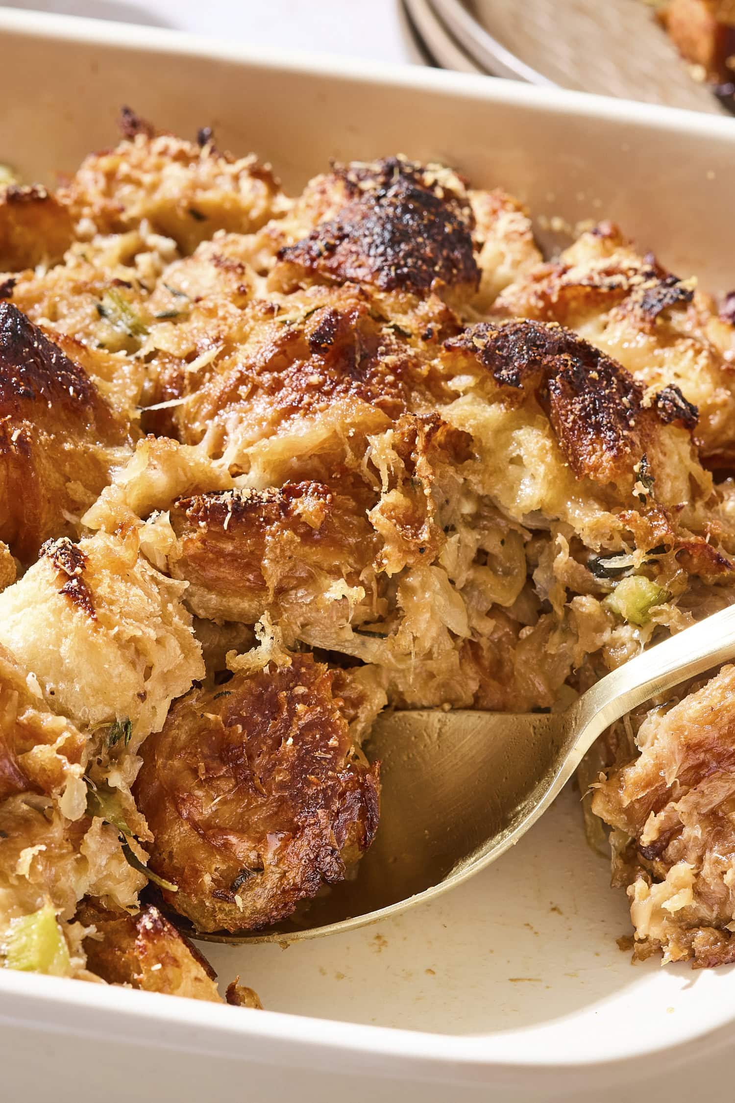 Spoon scooping up a serving of browned croissant stuffing in a baking dish.