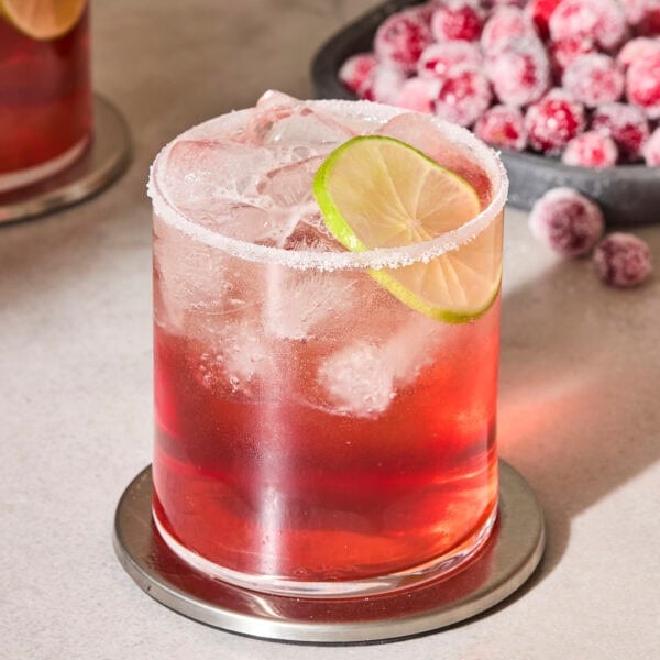 Glass with salted rim and lime wedge filled with a cranberry margarita.