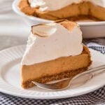 Slice of pumpkin pudding pie with a tall meringue topping with fork on plate.