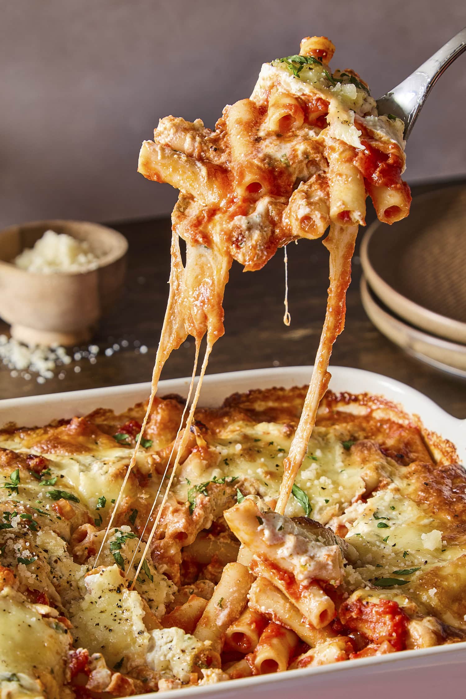 Serving of baked ziti being pulled from a casserole dish with a cheese pull.