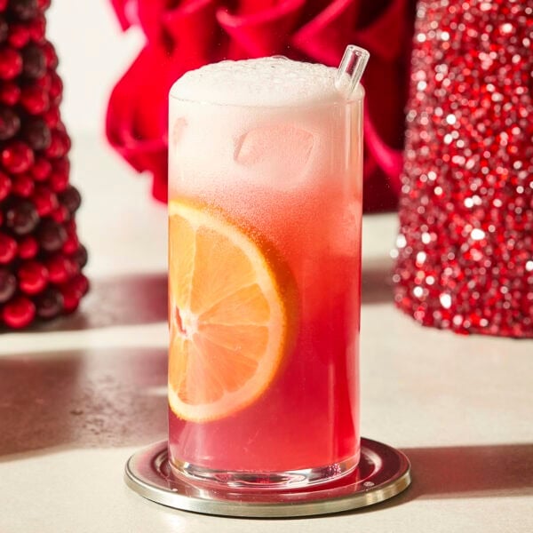 Tall glass with cranberry orange mocktail and an orange slice in the side.