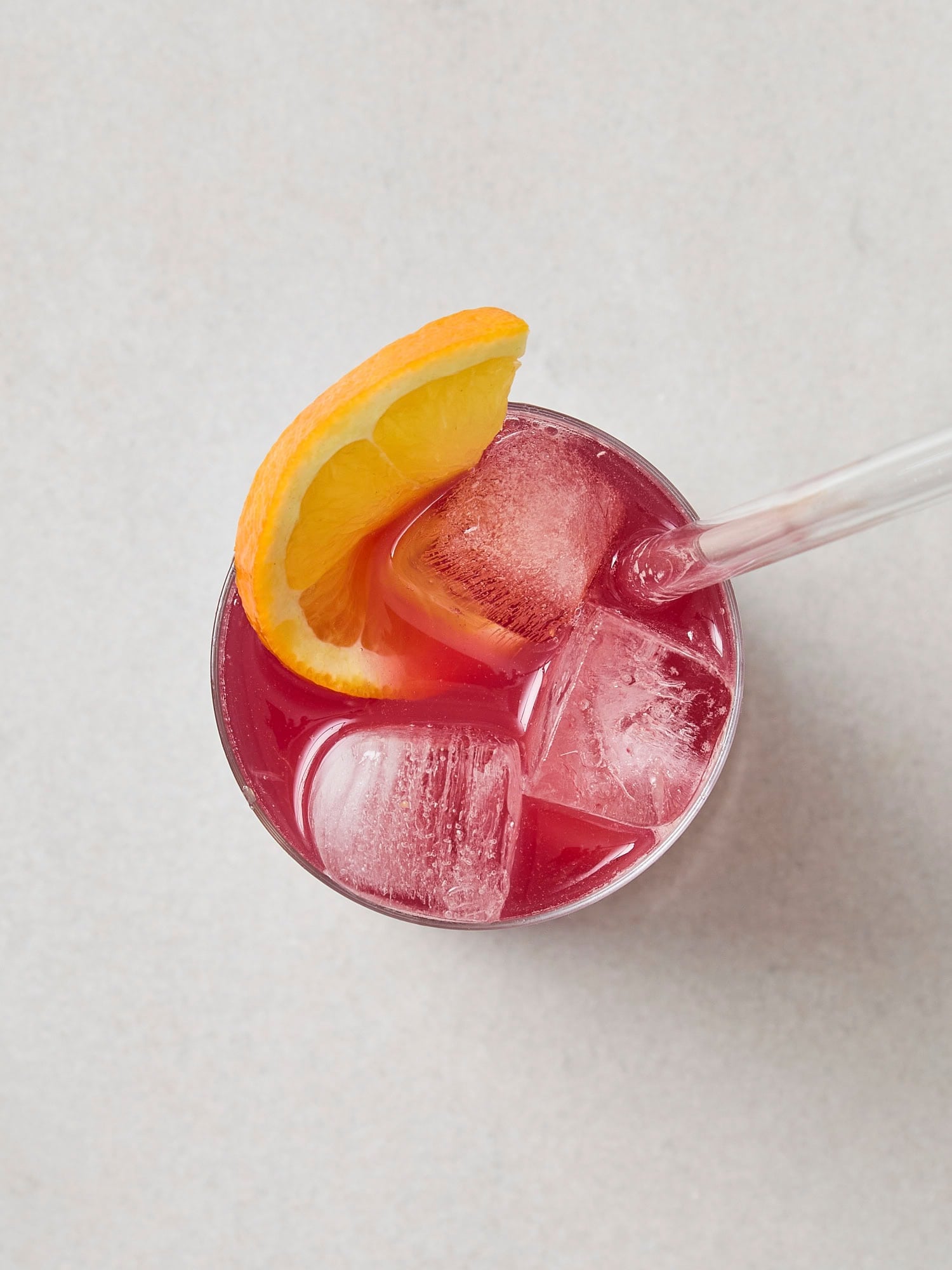 Glass with ice with pink mocktail liquid and orange slice on top.