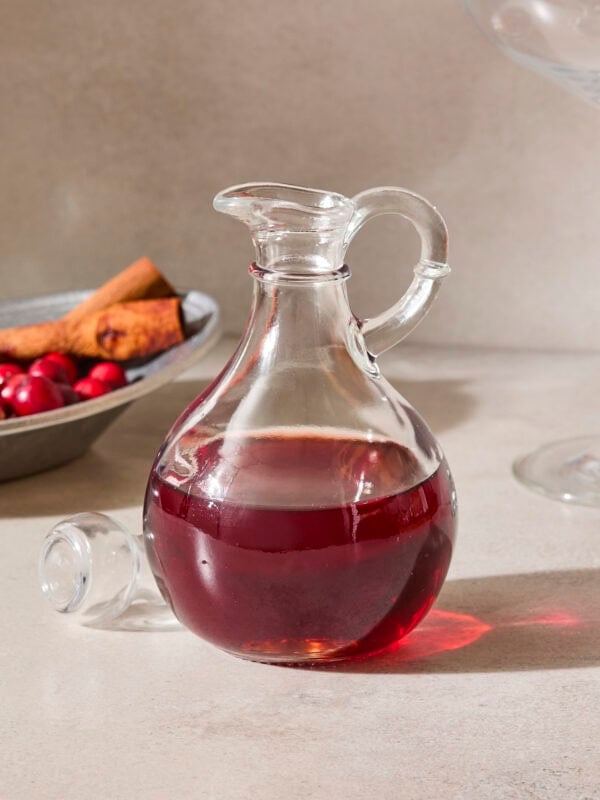Glass bottle filled with cranberry simple syrup with cinnamon sticks and cranberries in background.
