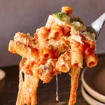 Spoonful of baked ziti with cheese pull handing below showing pasta.
