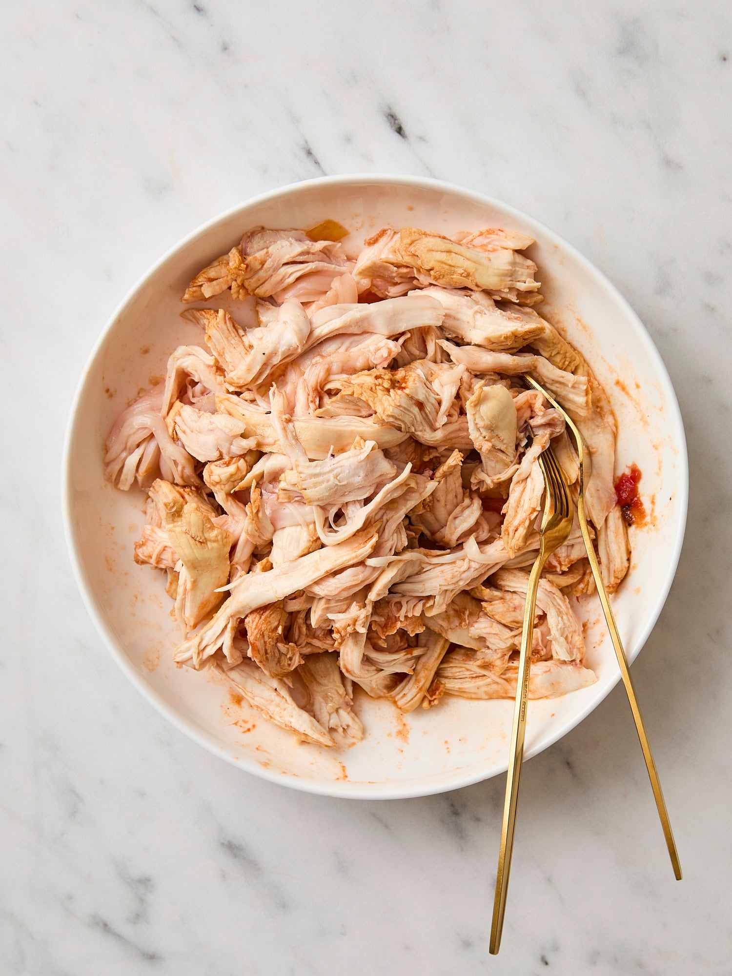 White bowl filled with poached shredded chicken.