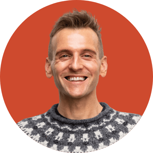 Kaleb Wyse wearing festive sweater smiling and standing in front of red background.