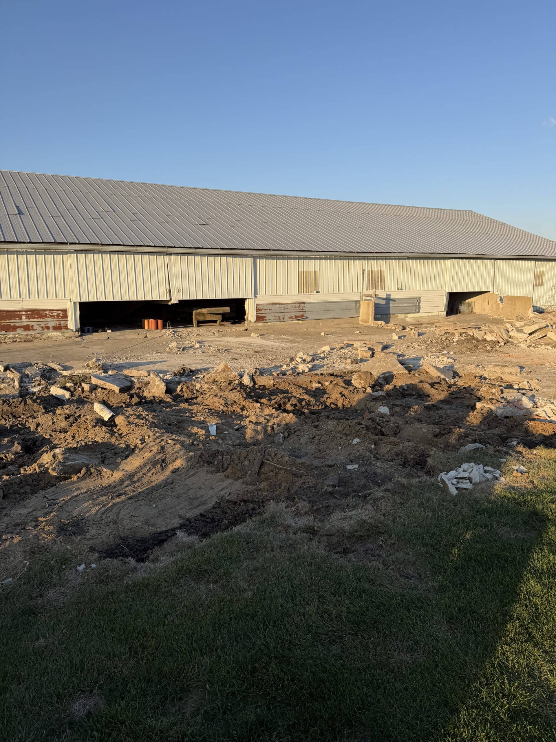 A farm building with lots of concrete removed and dirt piles in front.