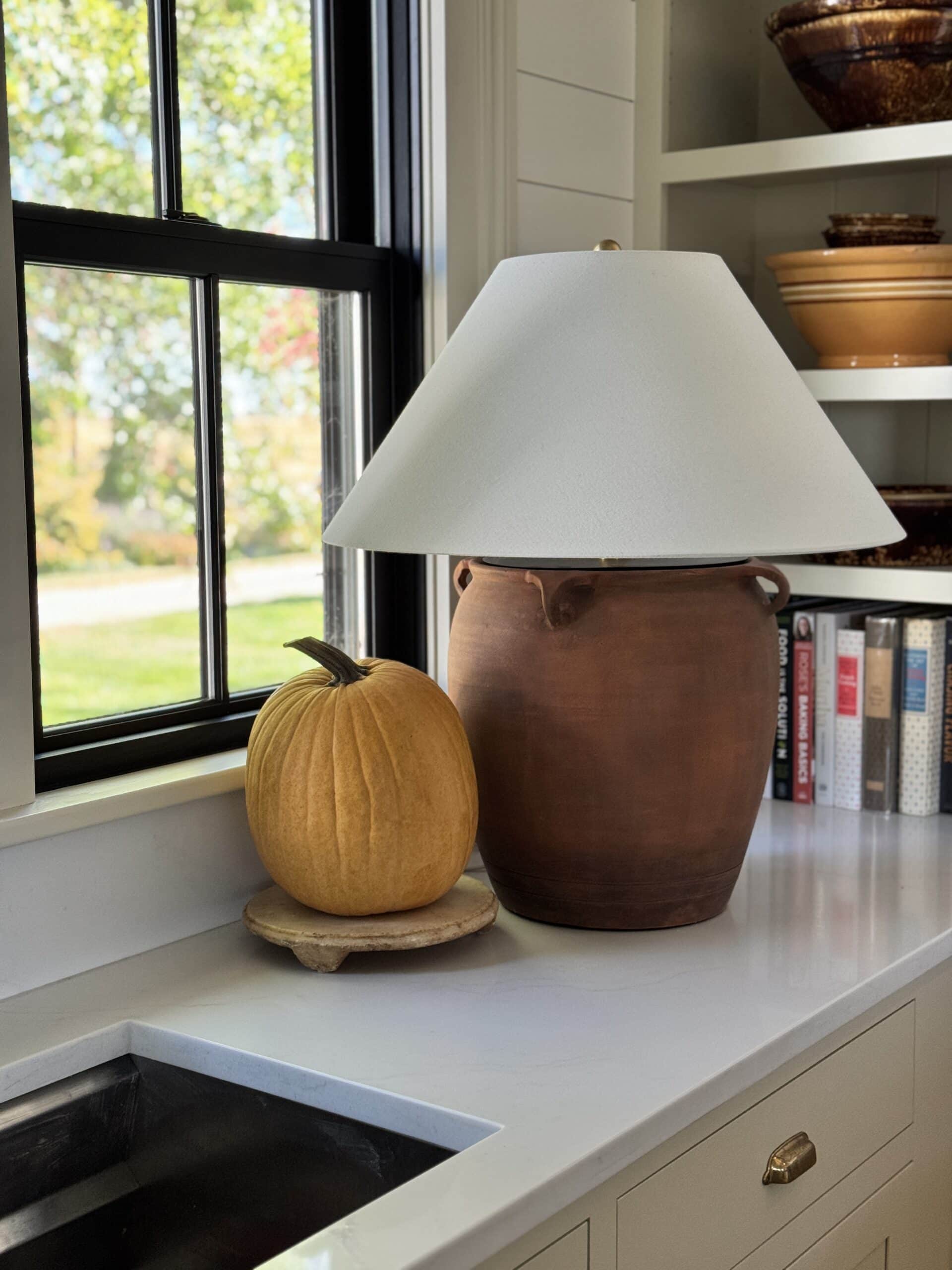 A lamp with a small yellow pumpkin beside it on a countertop.