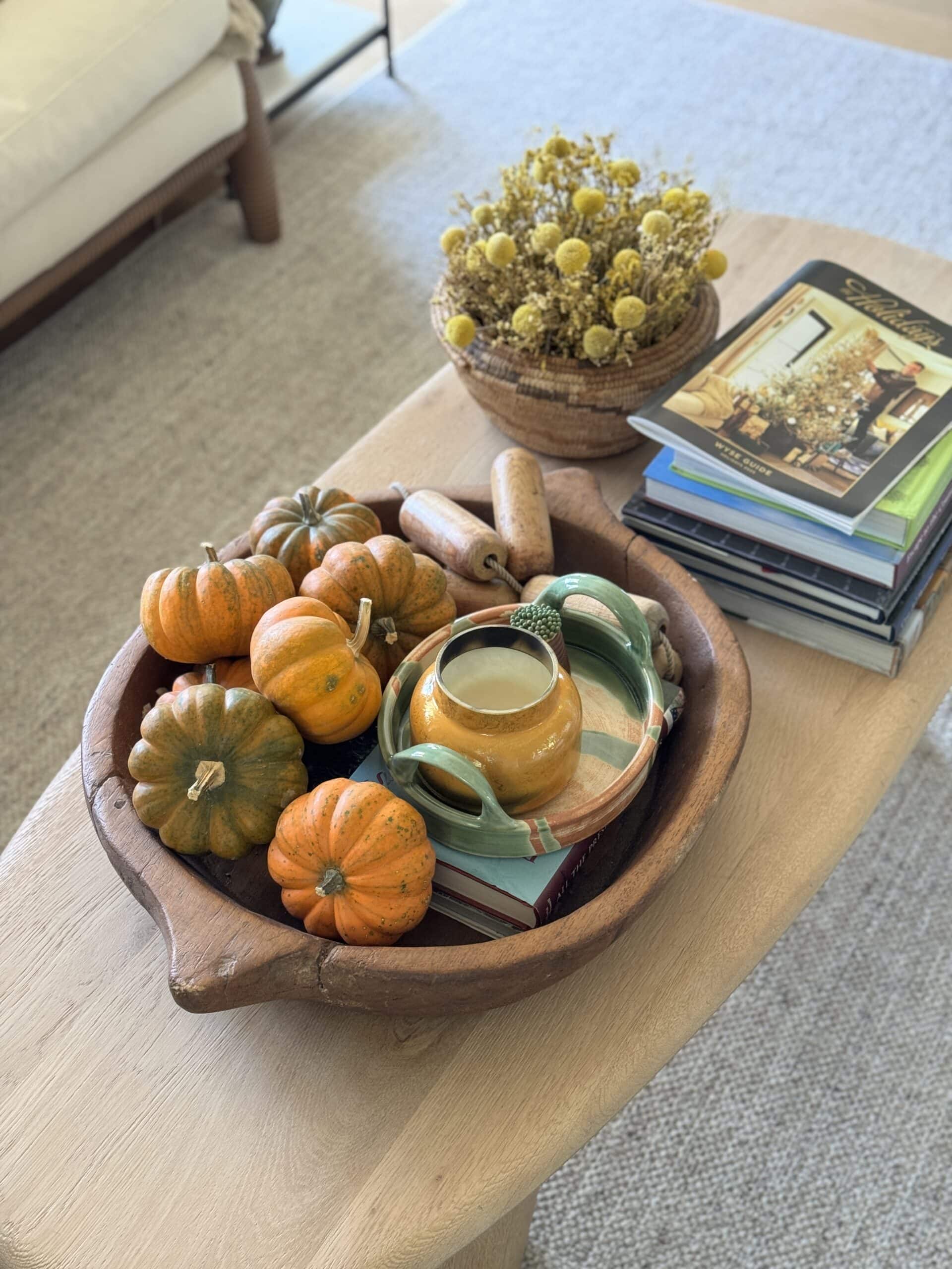 A wooden end table with fall decor including small pumpkins and a fall candle.