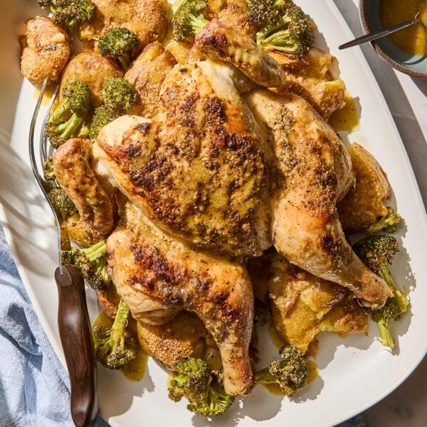 Whole roasted chicken with potatoes and broccoli on a platter.