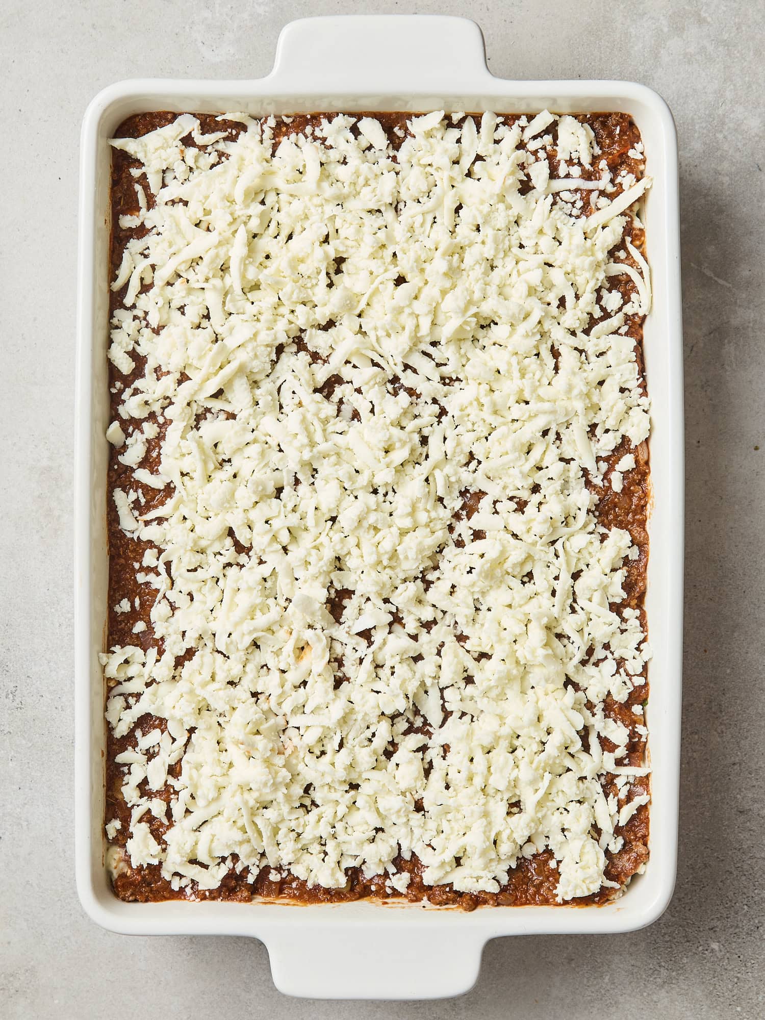 Unbaked lasagna with unmelted cheese on top.