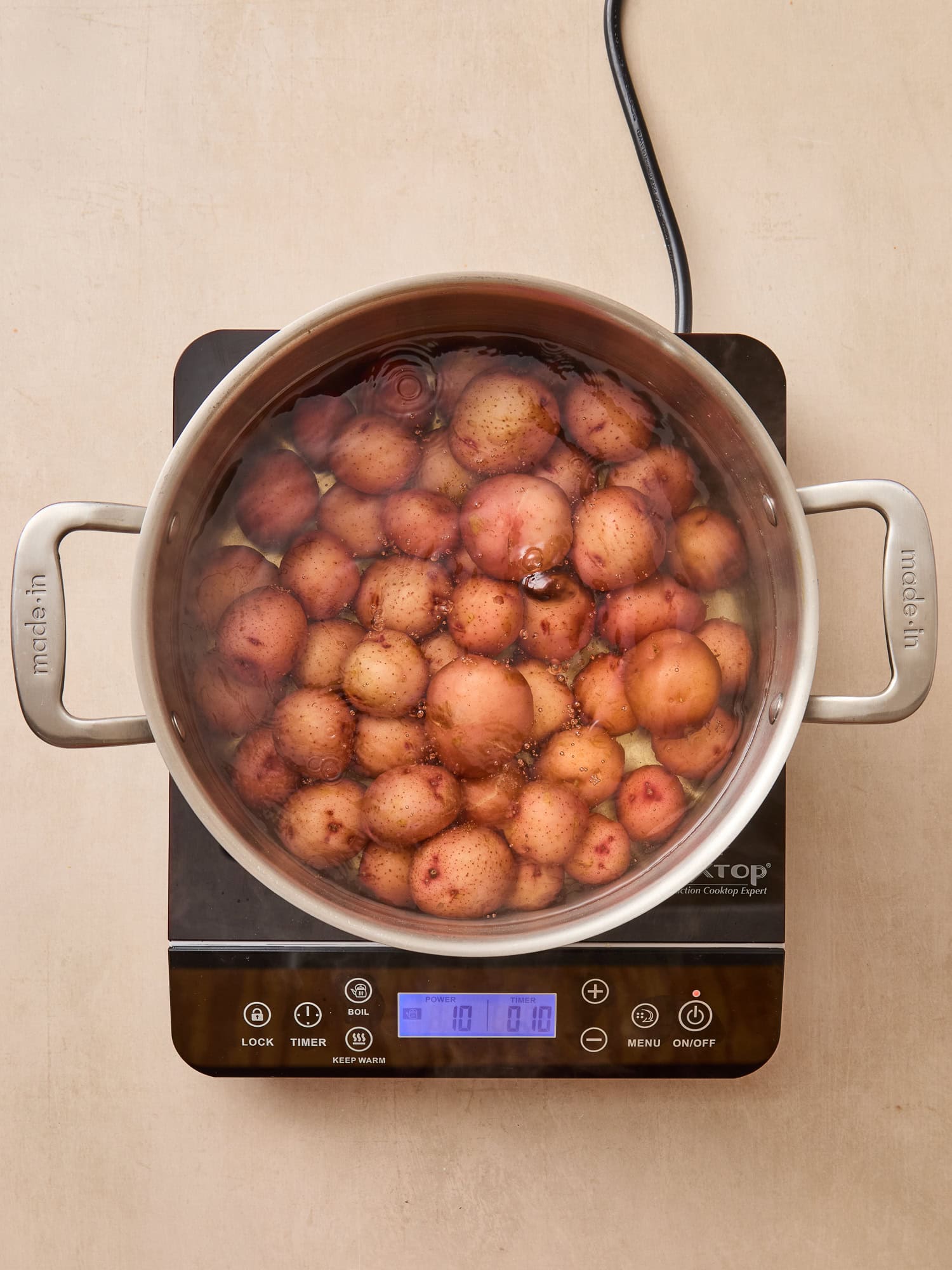 Potatoes cooking in a pot full of water on a cooktop.