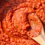 Wooden spoon stirring together easy marinara sauce in a pan.