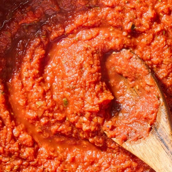 Wooden spoon stirring together easy marinara sauce in a pan.