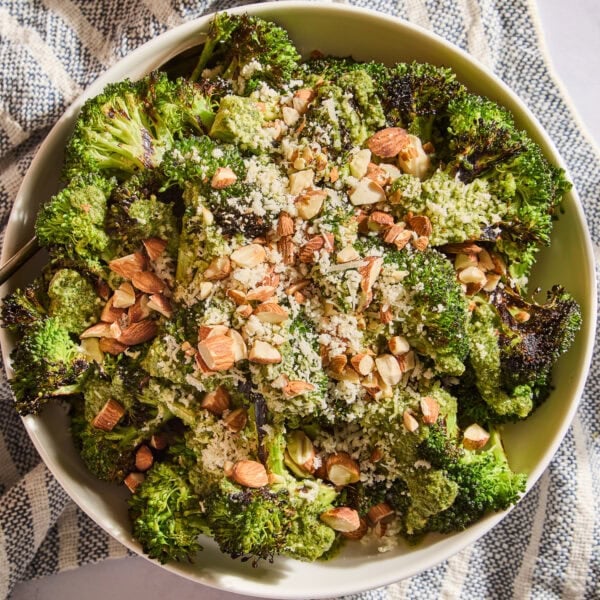 Grilled broccoli salad in a serving bowl topped with dressing, toasted almonds, and Parmesan cheese.
