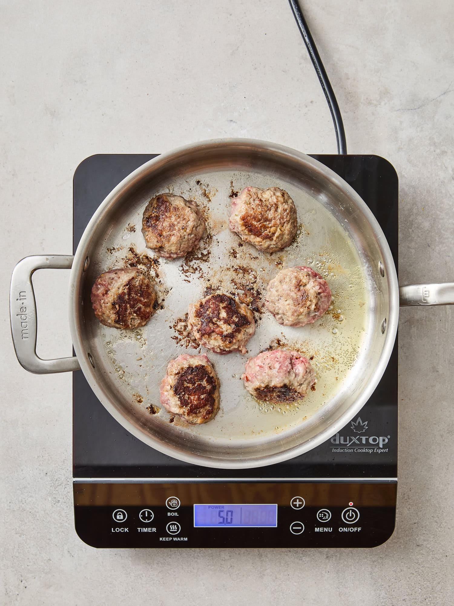 Meatballs brown in a pan.