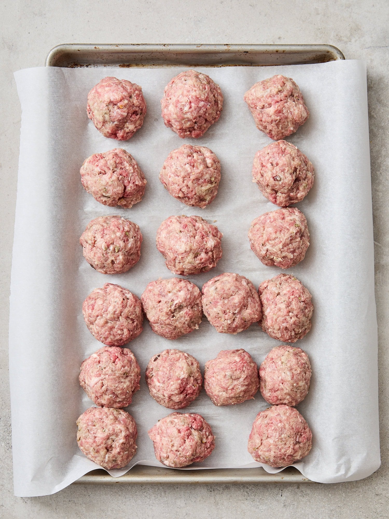 A baking tray lined with uncooked meatballs.