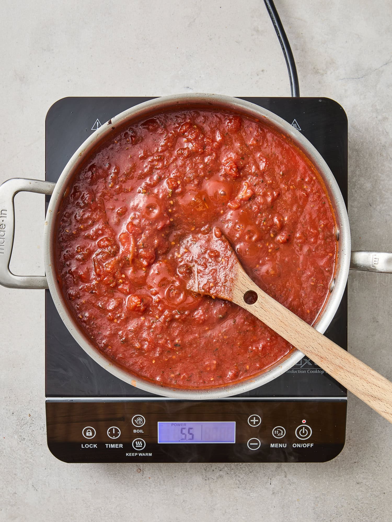 A pan with red sauce simmers on a stovetop.