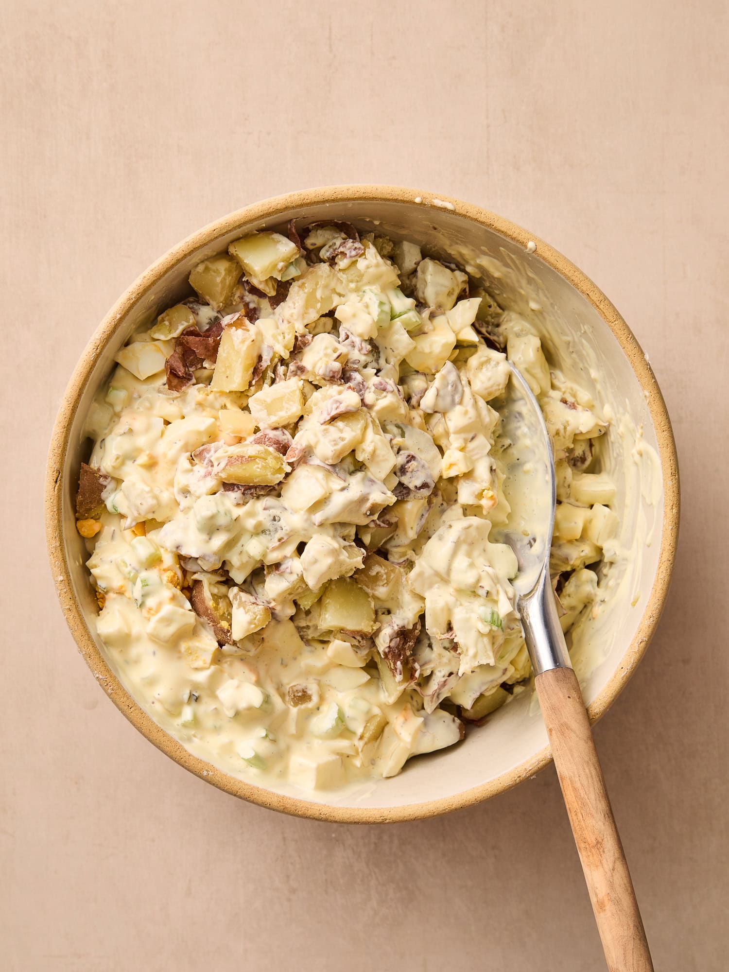 Mixing potatoes and dressing to assemble a potato salad.