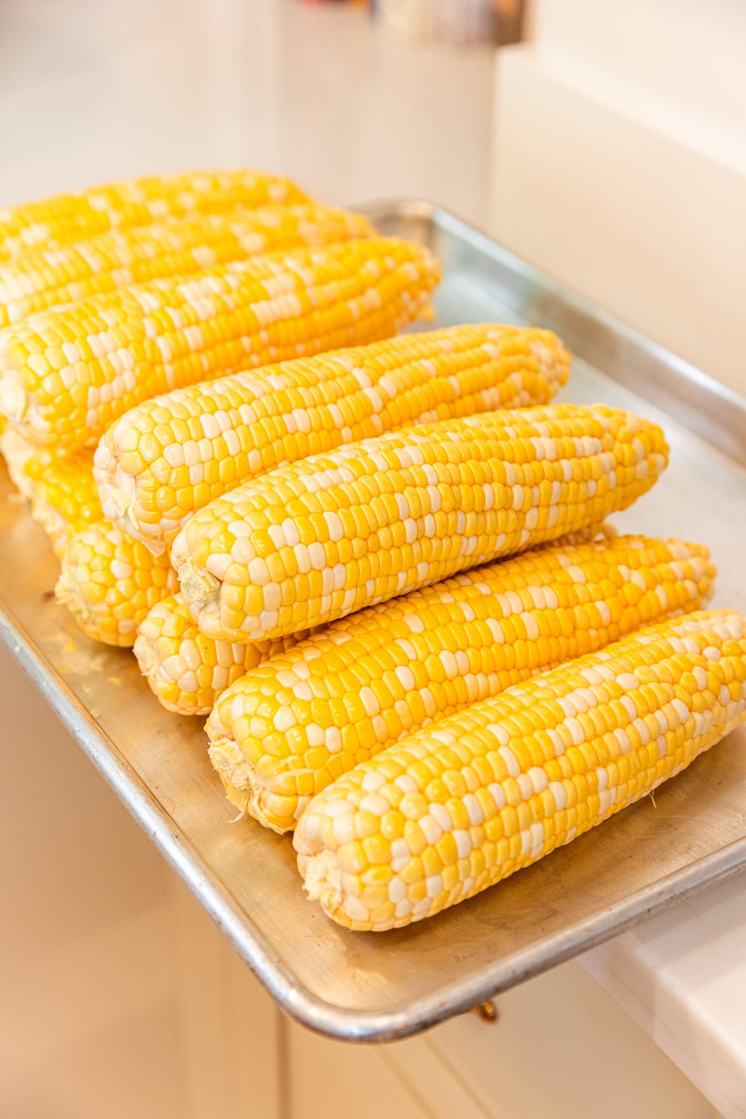 Shucked and cleaned ears of corn on baking sheet.
