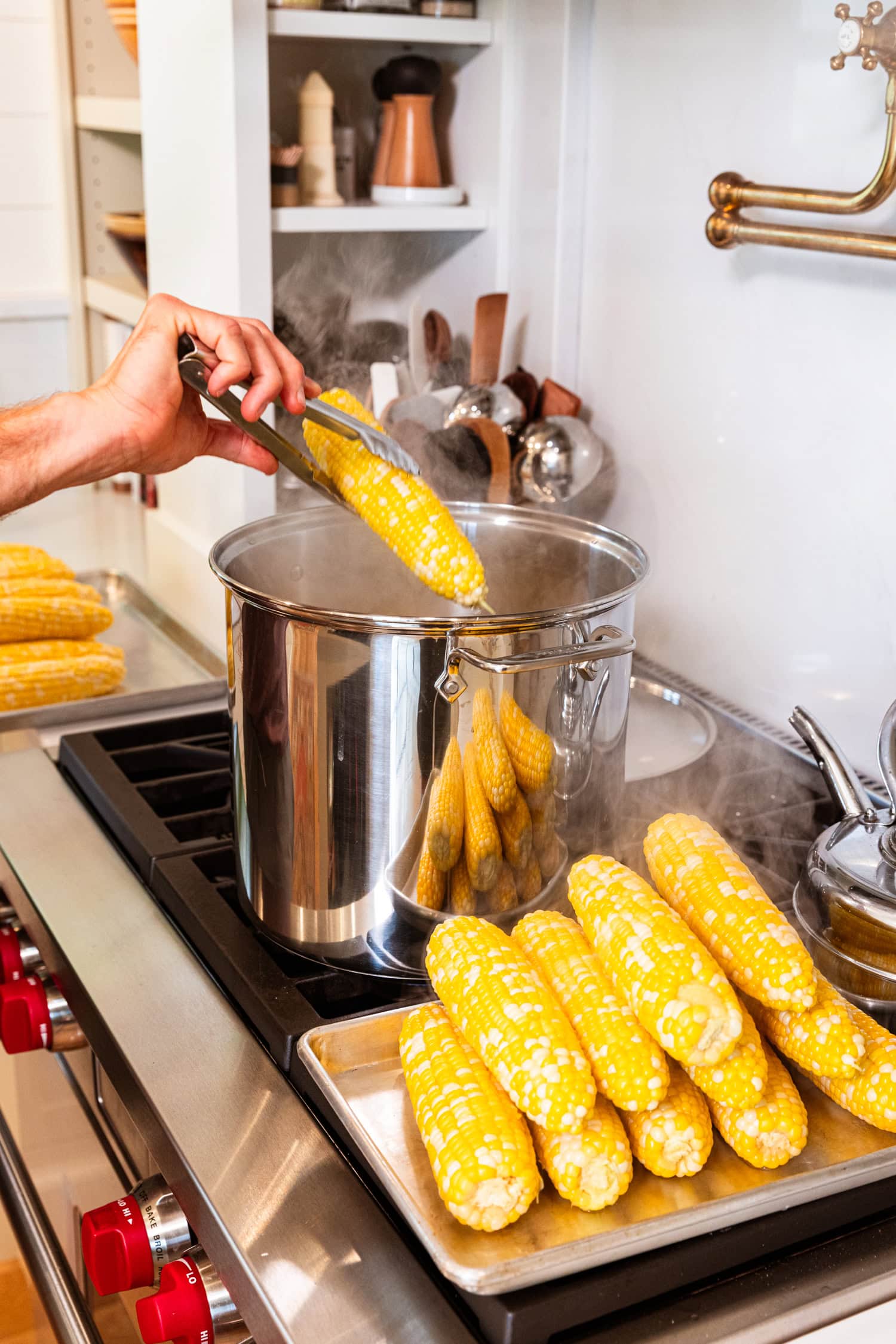 Tongs holding ear of corn over boiling water after cooking.