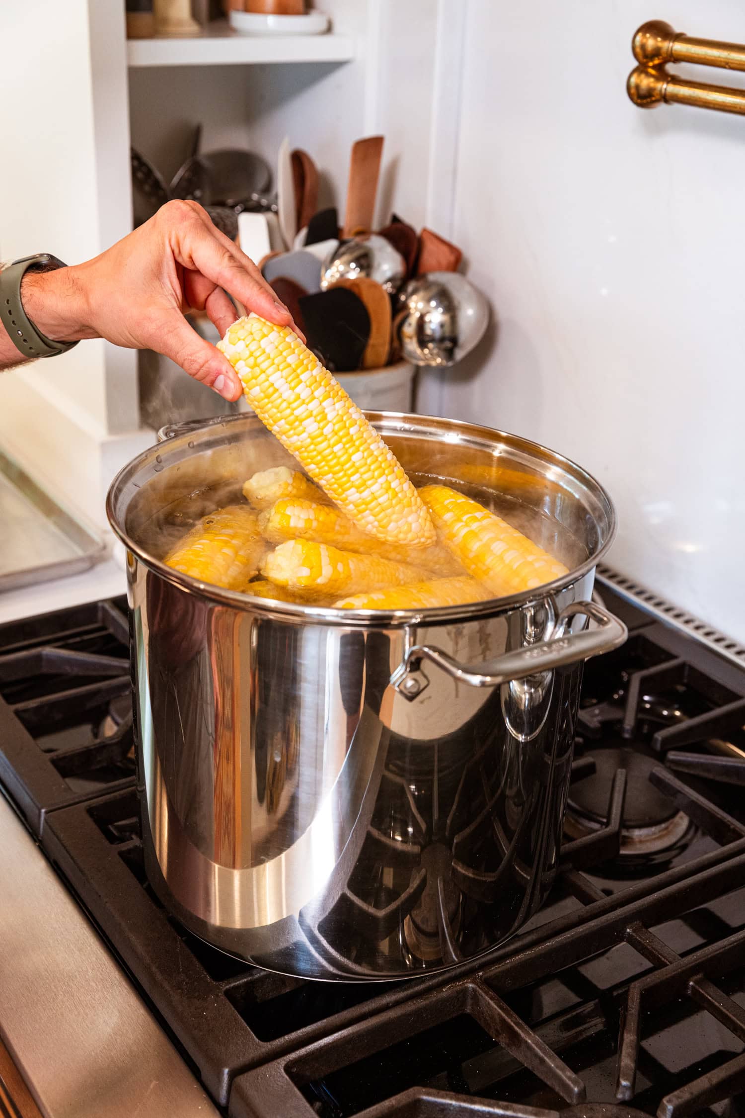 Ear of cleaned corn being placed in boiling water to be blanched.