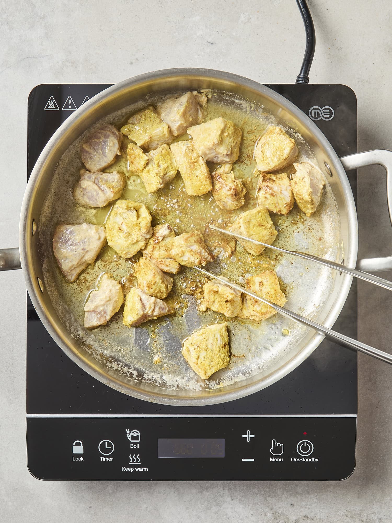 Chicken pieces with yellow tint from spices cooking.