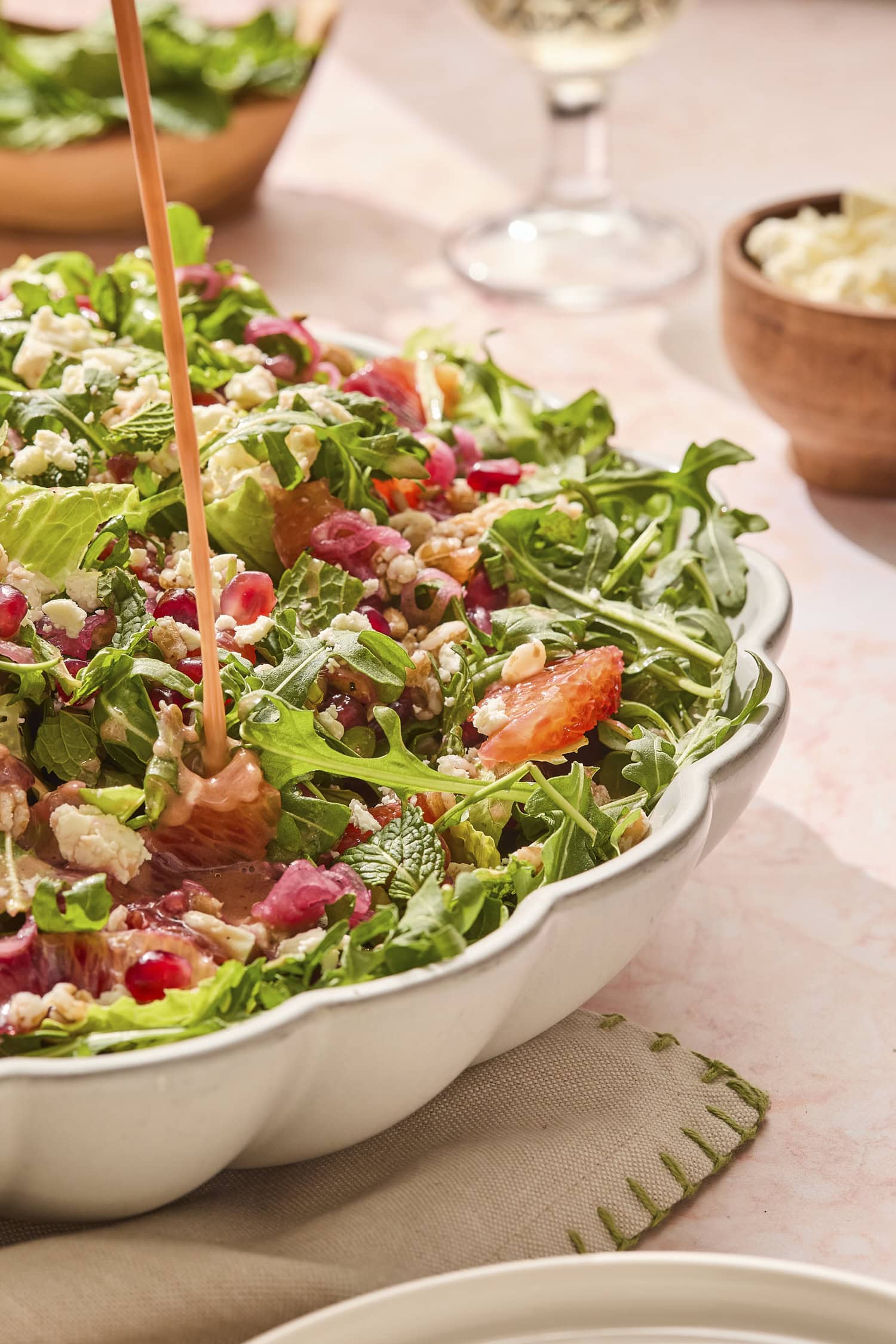 Farro salad with dressing being drizzled on top of blood orange segments on top of greens.