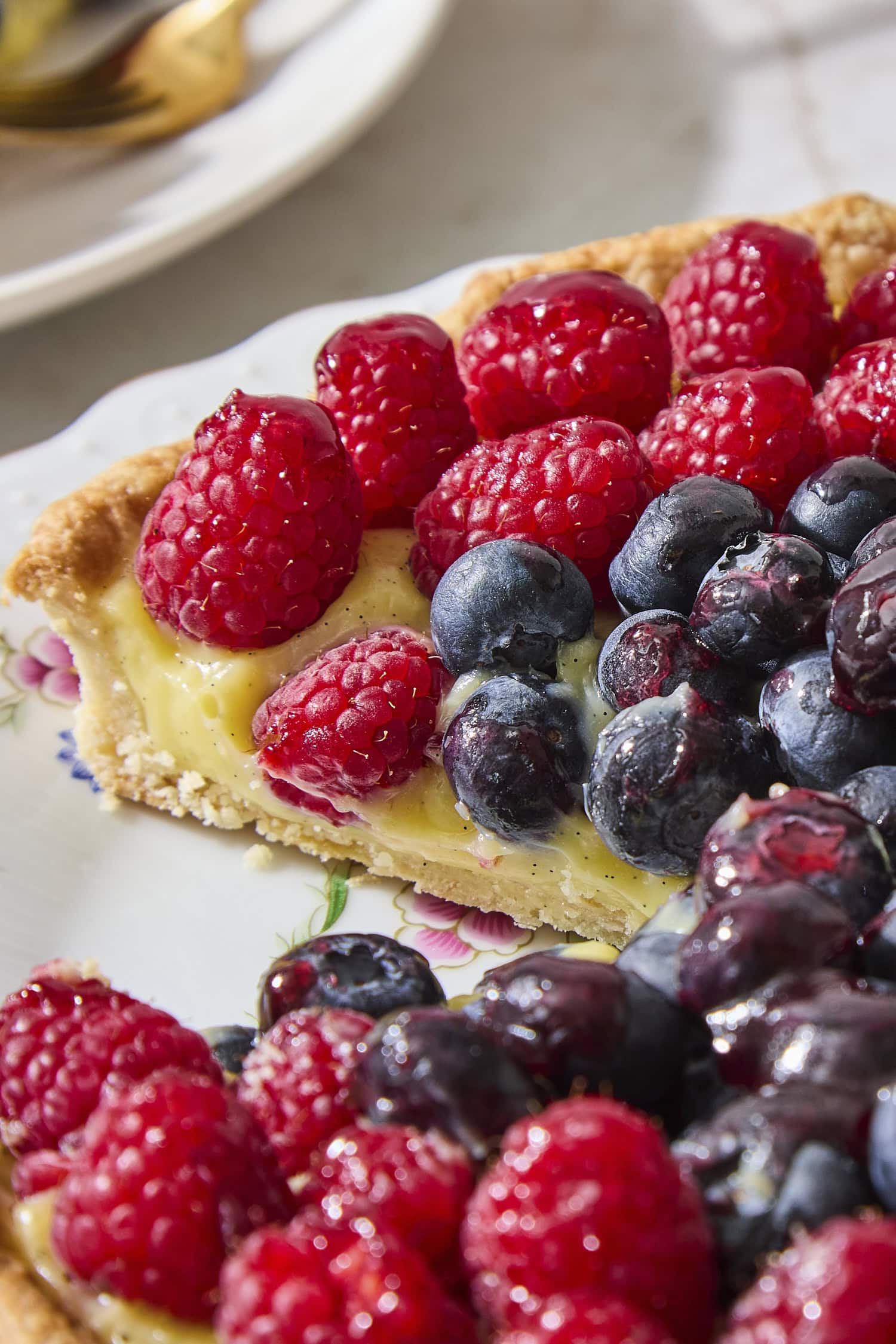 Slice taken out of a fresh fruit tart with pastry cream filling and berries on top.