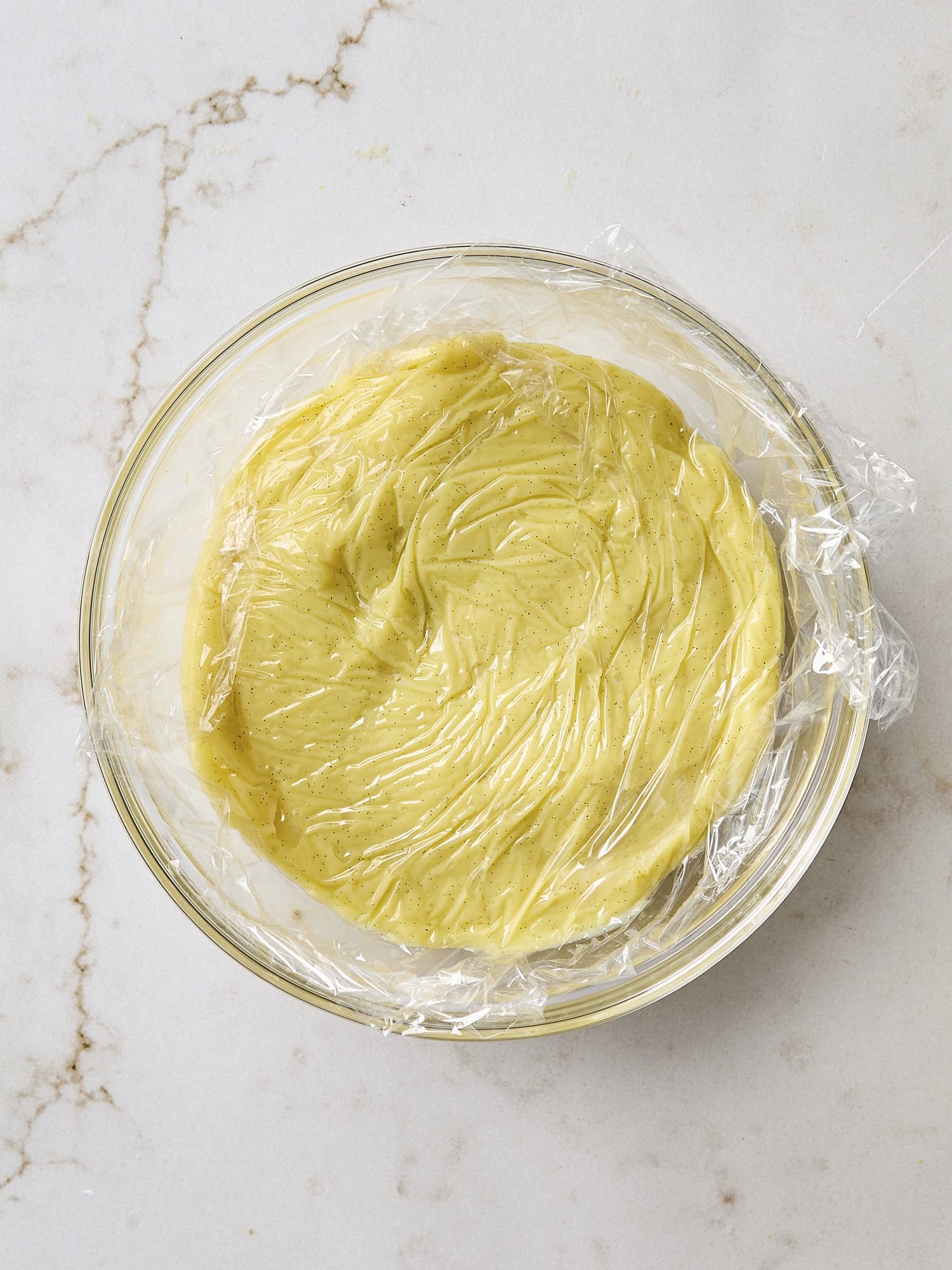 Cooling pastry cream mixture with plastic on top.