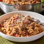 Parmesan cheese being sprinkled over the top of a serving of beef ragu pasta.