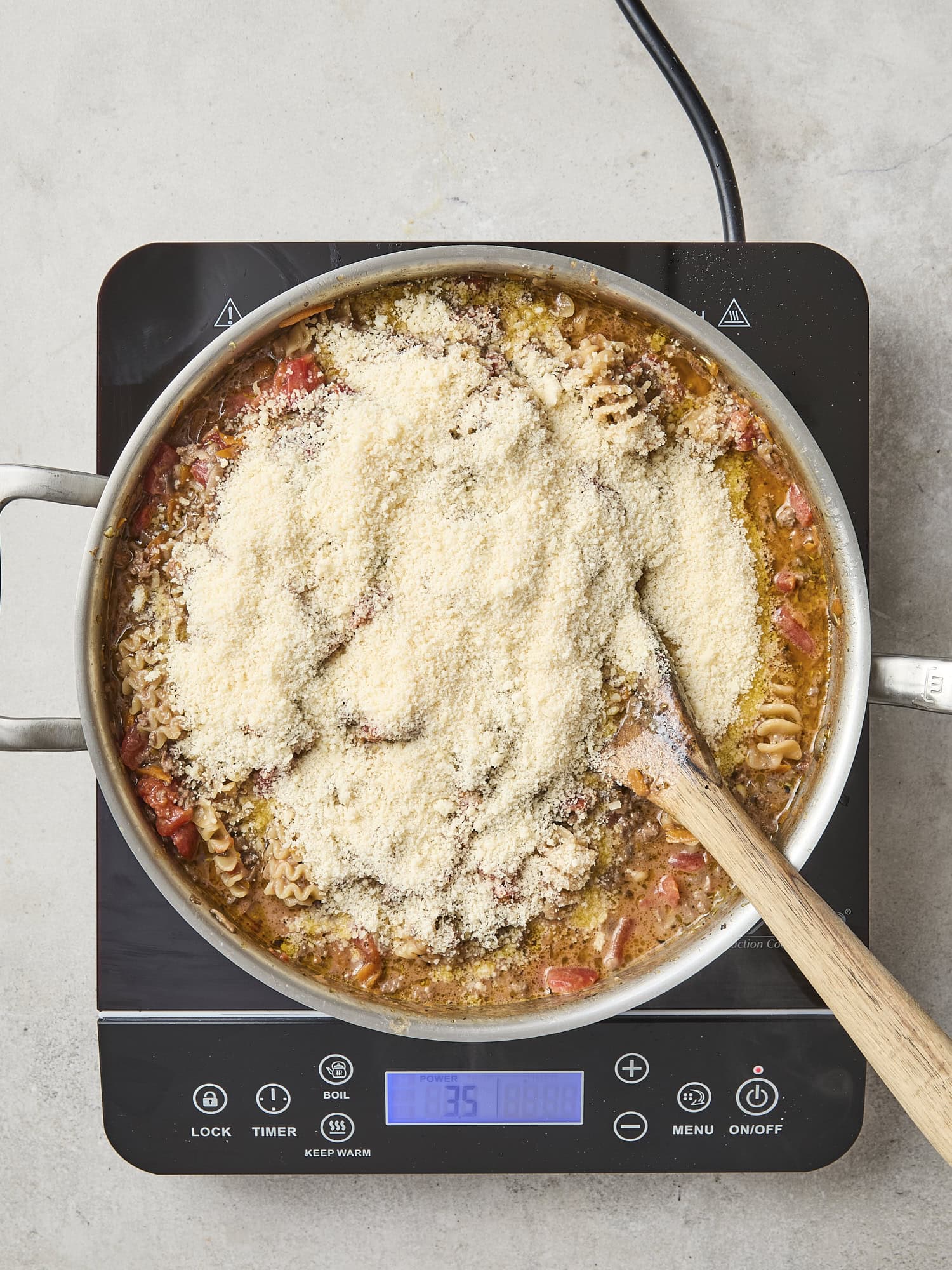Skillet with Parmesan cheese on top of cooking ragu.