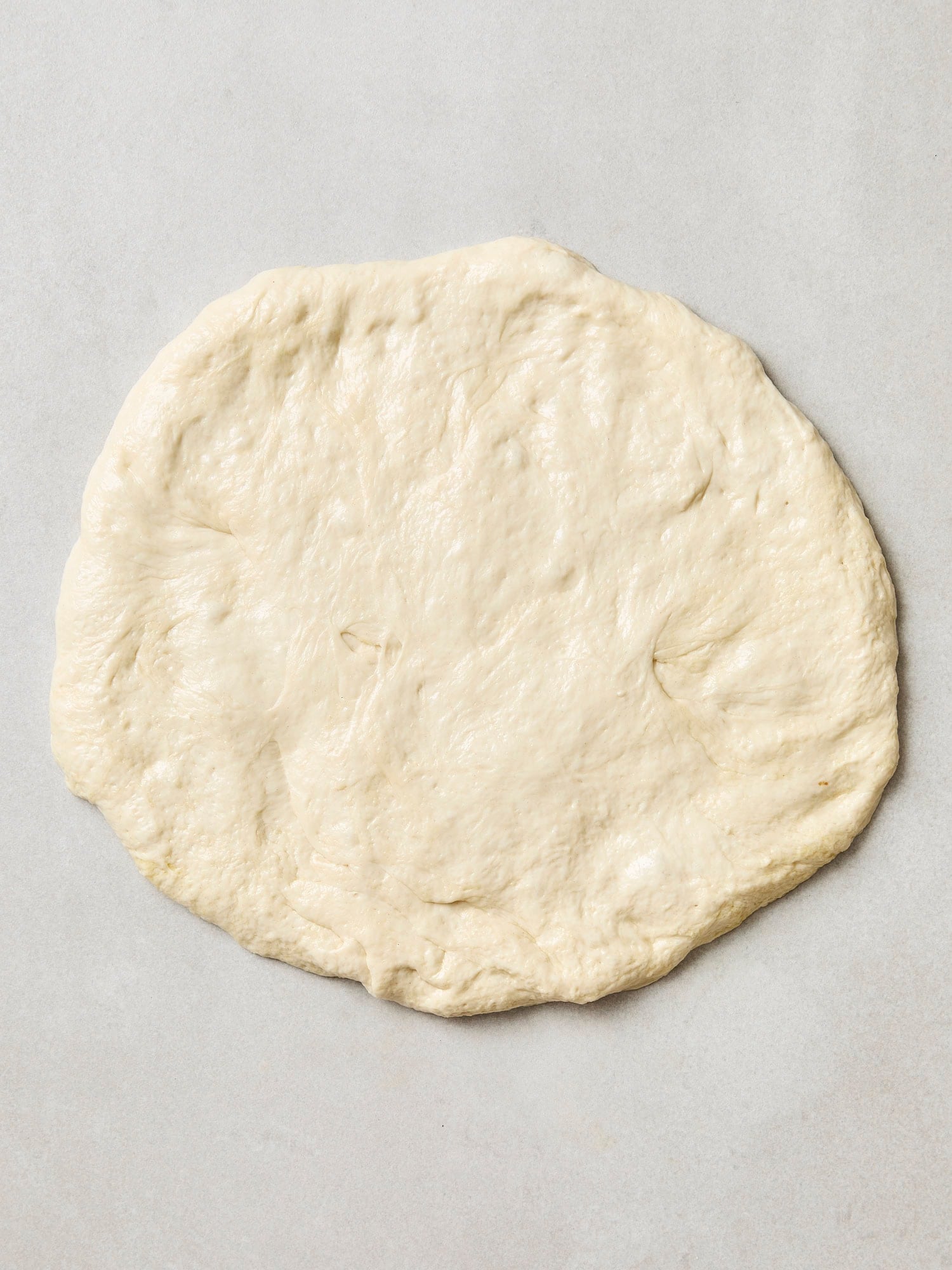 Pizza dough pressed out into a rough circle.