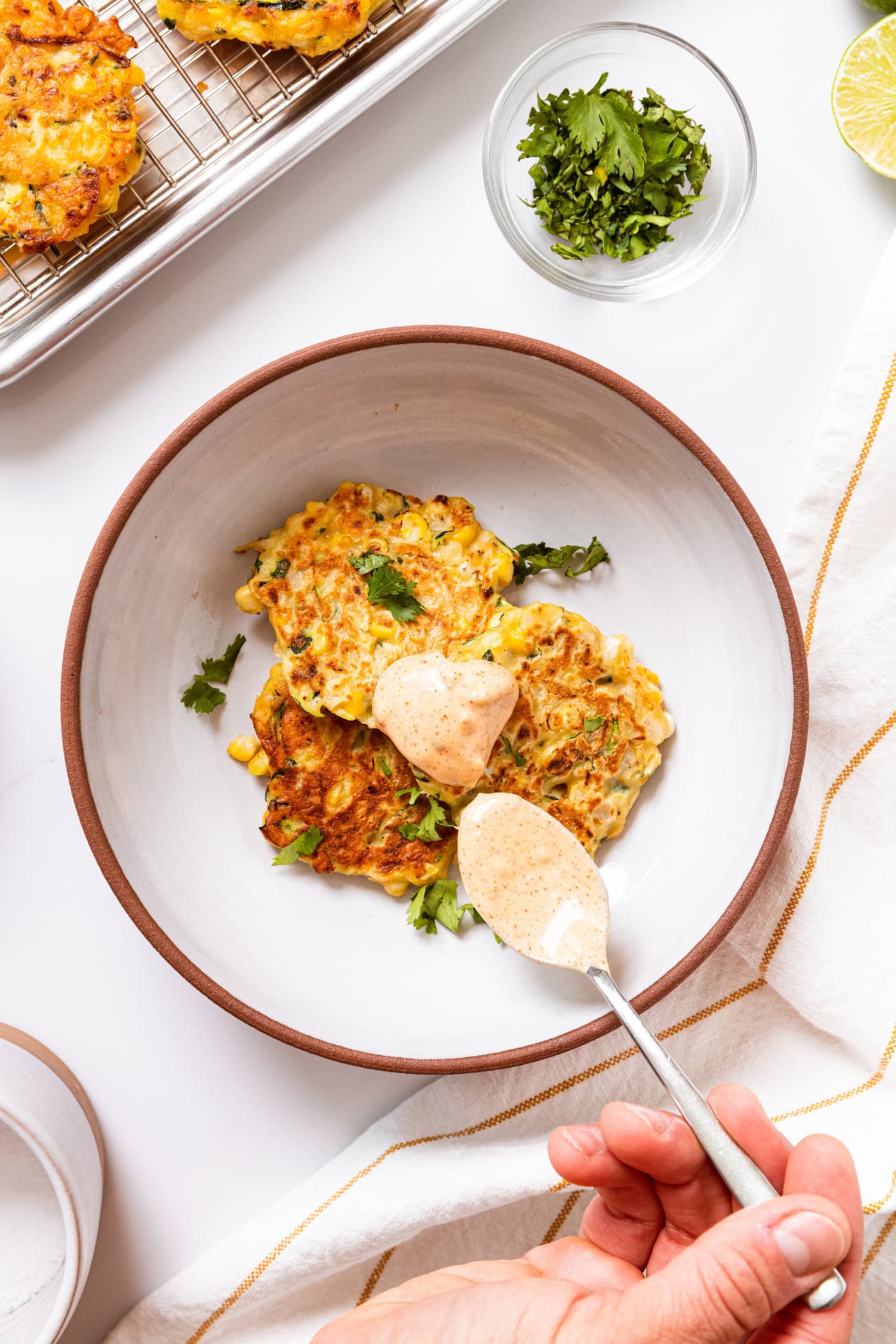 White bowl with three corn fritters topped with cilantro and spoonful of chipotle mayonnaise sauce all on white countertop.