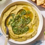 Bowl of creamy avocado hummus with cilantro sauce on top.