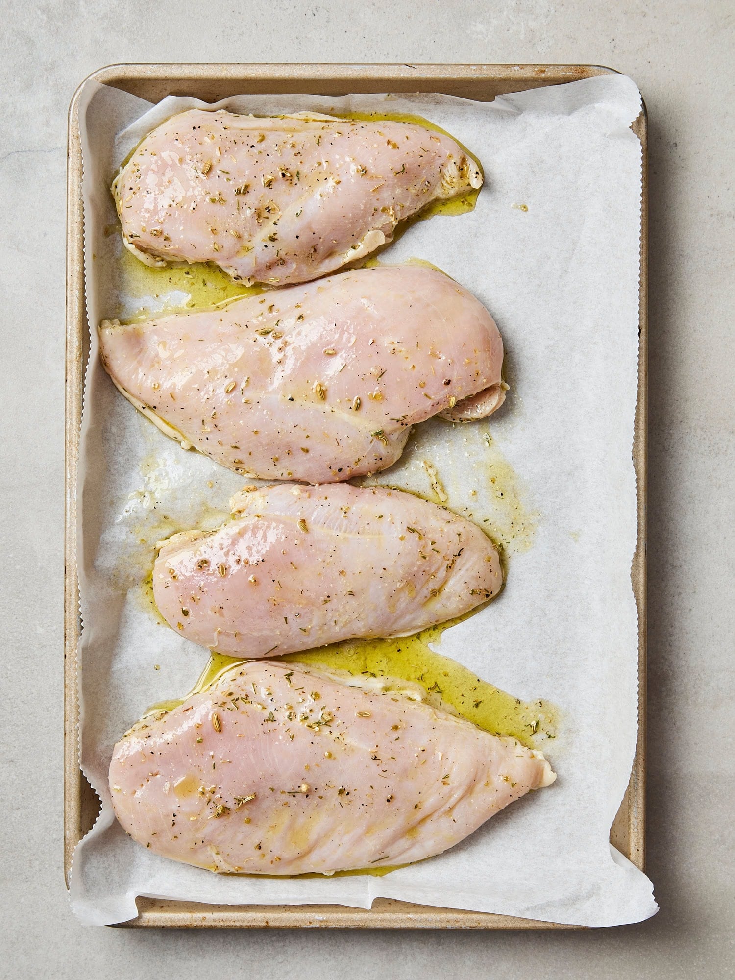 Uncooked chicken breast pieces on parchment-lined baking sheet before baking.