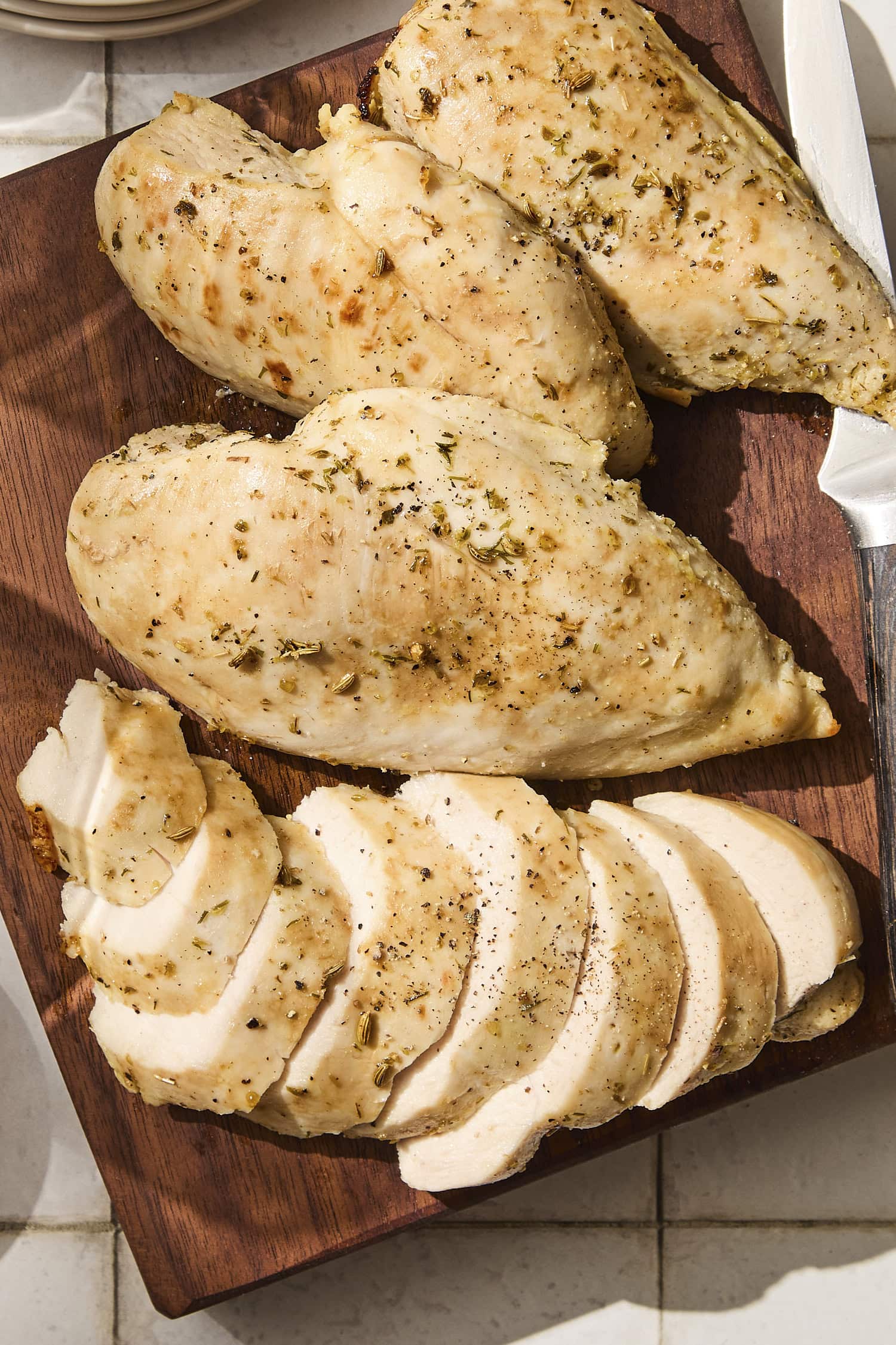Sliced pieces of chicken breast on cutting board with pepper on top.