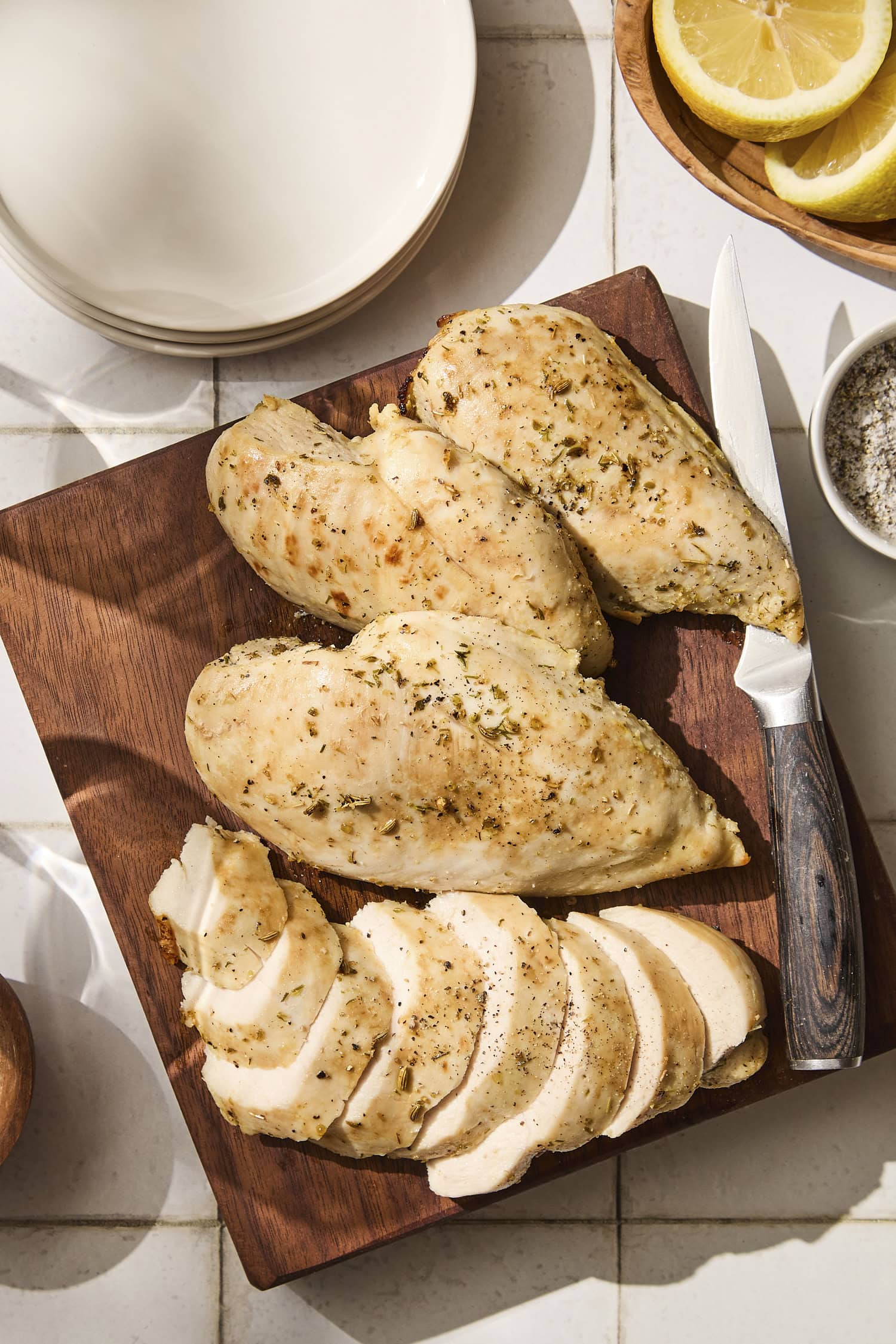 Four baked chicken breasts with one sliced with lemon herb marinade.