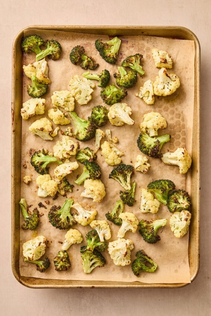 Broccoli and cauliflower on a parchment-lined baking sheet after roasting.