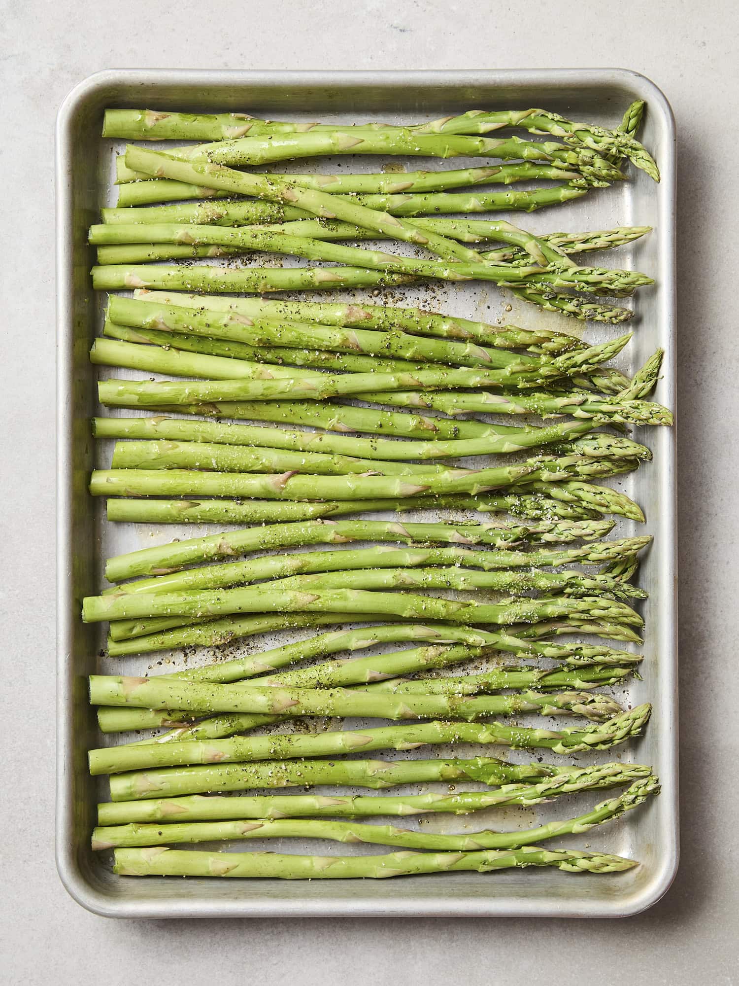 Asparagus on sheet pan with salt and black pepper.
