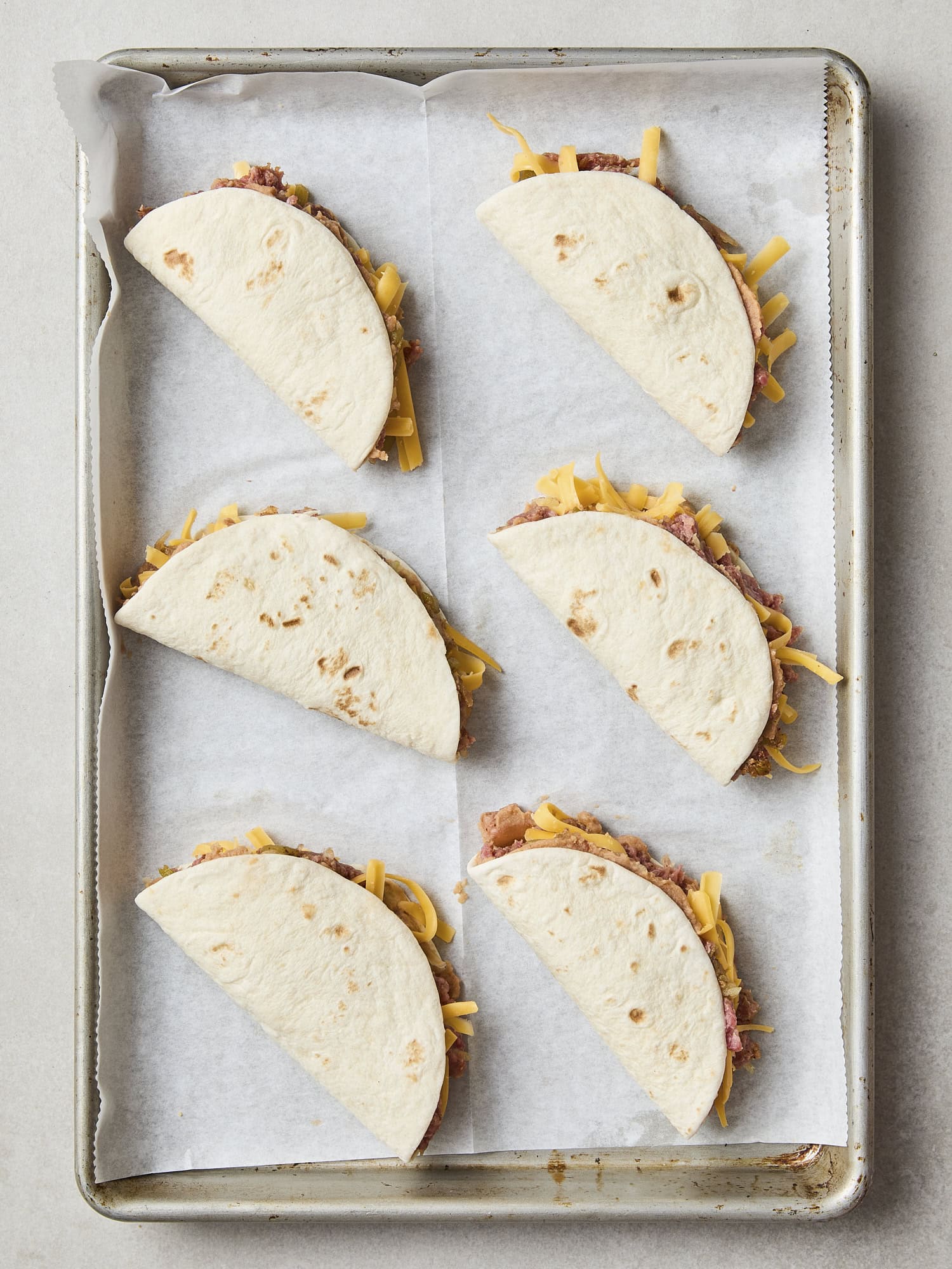 Unbaked beef tacos with cheese and filling spilling out.